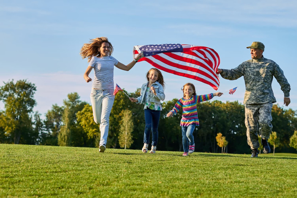 Military family running on the lawn with an American flag.